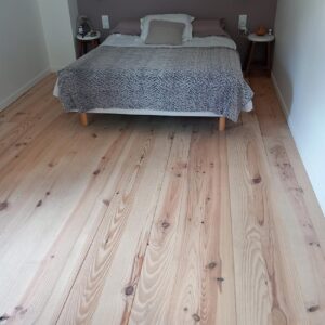 Chambre élégante avec grand lit gris sur parquet clair en bois, murs gris et blancs. Deux tables de chevet avec lampes.