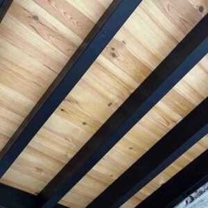 Plafond moderne en bois clair avec poutres sombres diagonales créant un contraste saisissant. Design intérieur contemporain.