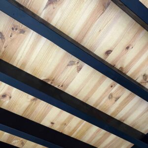 Plafond ou sous-face en bois clair avec des planches horizontales et des poutres sombres verticales créant un contraste.