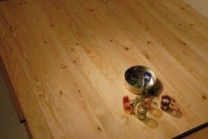 Plancher en bois clair à lames, motifs naturels et nœuds. Décoré d'un plateau métallique, de six verres colorés et de fleurs.