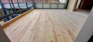 Plancher en bois clair neuf dans une pièce en rénovation avec garde-corps métallique et vue sur des toits en tuiles.