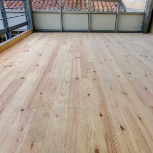 Plancher bois clair neuf sur mezzanine, vue sur tuiles de toit et balustrade métallique. Espace intérieur en rénovation.