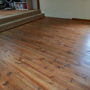 Plancher en pin rustique verni et patiné, menant à deux marches basses recouvertes de moquette beige dans un espace de bureau ouvert.