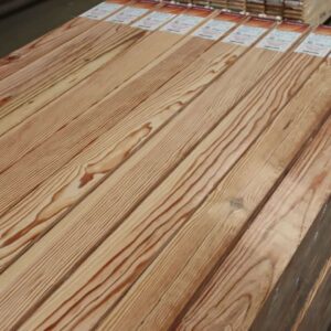 Pile de planches de bois clair avec grain prononcé, emballées individuellement. Étiquettes produit CE visibles, prêtes à l'emploi.