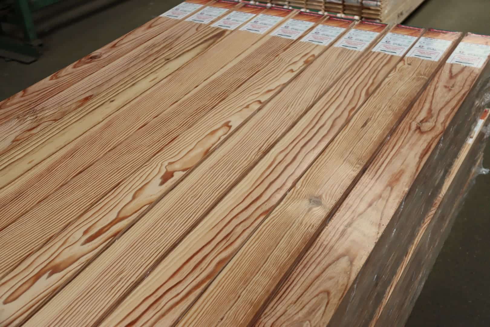 Pile de planches de bois clair avec grain prononcé, emballées individuellement. Étiquettes produit CE visibles, prêtes à l'emploi.