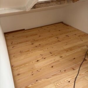 Plancher en bois clair neuf posé dans une pièce aux combles aménagés, avec lames de pin et poutre apparente.