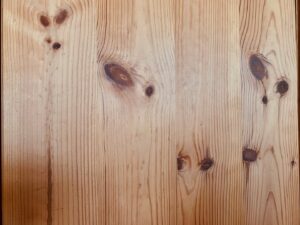 Panneau de bois clair avec grain vertical et plusieurs nœuds foncés, texture naturelle et chaude.