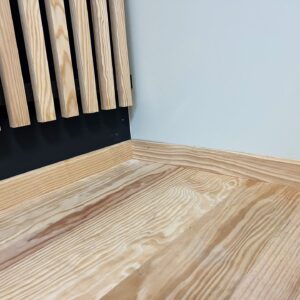 Coin de pièce moderne avec panneaux muraux en lattes de bois clair, sol en parquet de pin à grain visible et plinthes assorties sur murs noir et bleu pâle.