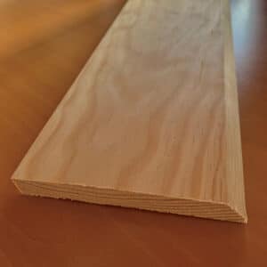 Planche de contreplaqué clair avec grain visible et couches. Une extrémité est droite, l'autre biseautée en coin, posée sur une table en bois.