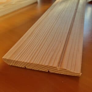 Planche de bois brut avec grain visible, présentant un côté arrondi et un profil rainuré. Idéal pour moulure ou finition intérieure.
